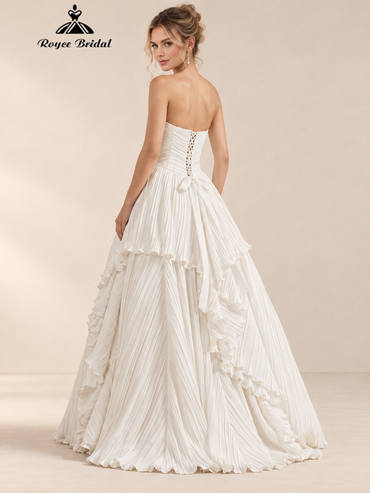 Back view of an ivory A-line wedding dress with a lace-up back, pleated skirt and train.